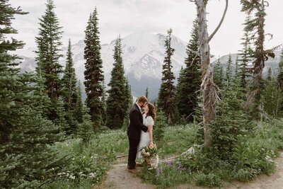 Couple embracing in a mountain area with Mount Rainier visible in the background.