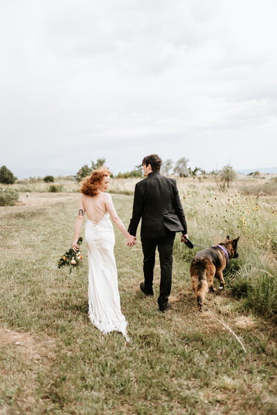 bride and groom running through field with their dog