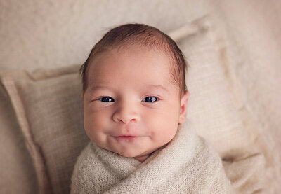 A content baby smiles brightly while being wrapped in a warm, soft blanket.