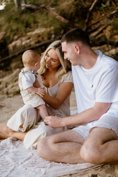 Family looks lovingly at baby while sitting on the beach - Natural family photoshoot