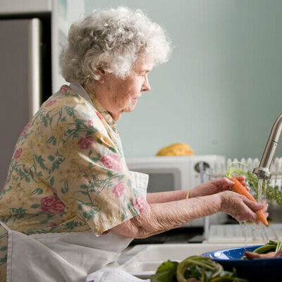 Senior woman in the kitchen of her house, washing vegetables