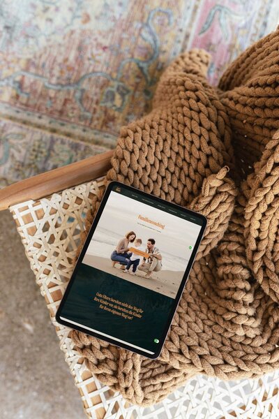 Tablet mit Website-Design für Familiencoaches, stilvoll inszeniert auf Stuhl mit Strickdecke.