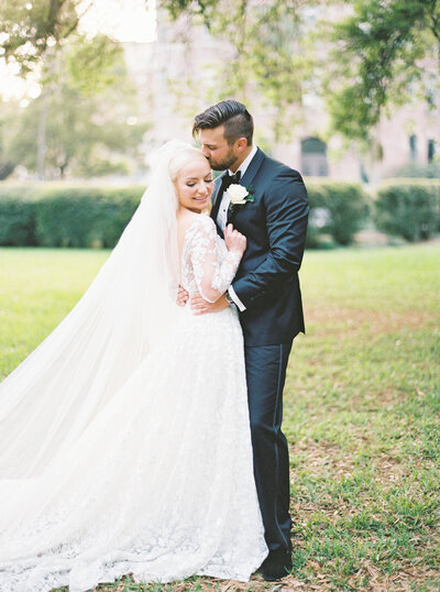 Bride looking into the camera smiling while groom kisses her temple oxford exchange wedding photographer in Tampa