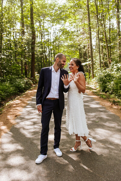 Elopement in Maine. Dominican couple taking portraits at a beautiful outdoor space with a walkway of tall trees on both sides of them.