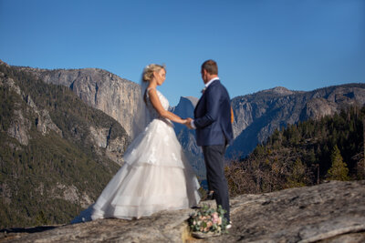 A bride and groom exchange vows atop a scenic overlook during their Yosemite elopement, with El Capitan and the valley stretching behind them. Captured by Yosemite elopement photographers, this intimate ceremony highlights the beauty of saying 'I do' in the mountains.