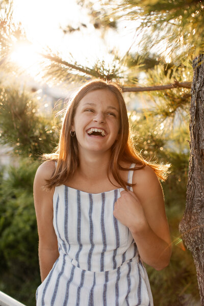 Senior sits in a tree, smiling up at the sky