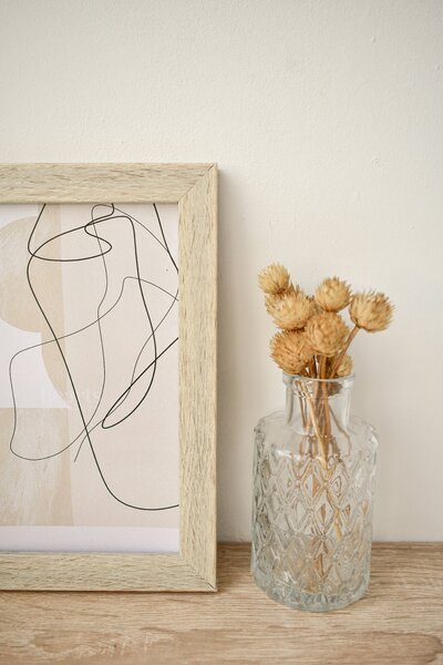 Vase of dried flowers and framed abstract art sitting in front of a white wall