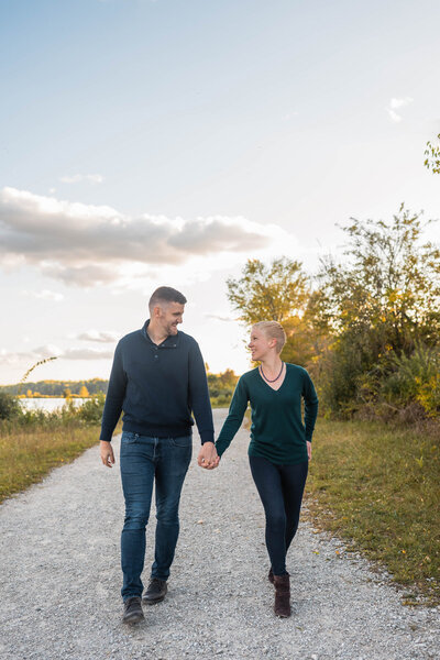 Bride and groom hold hands in front of tall trees at sunset