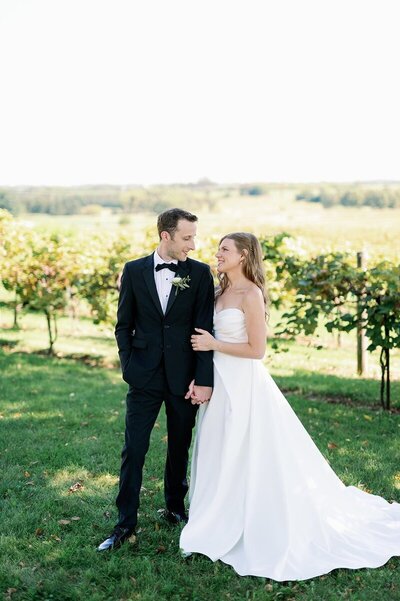 wedding photographers in minneapolis capturing bride and groom holding hands and looking at each other lovingly in front of a trees