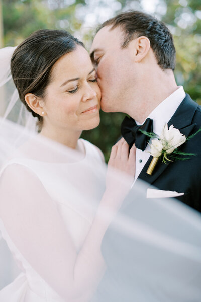 groom kissing his bride on the cheek during their luxury wedding photography portraits