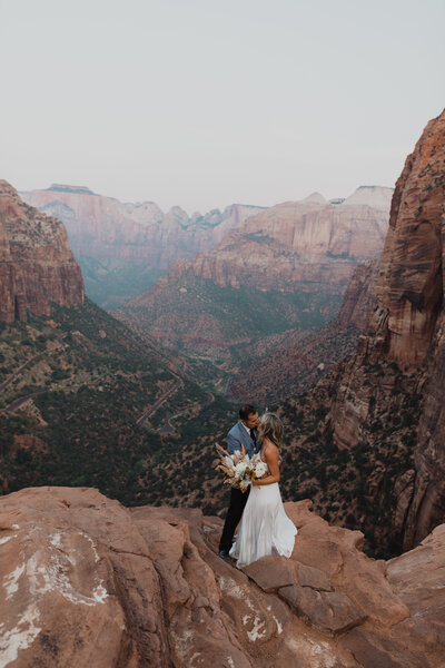 Wedding couple stands in front of a canyon in Zion National Park during a sunrise elopement in Utah