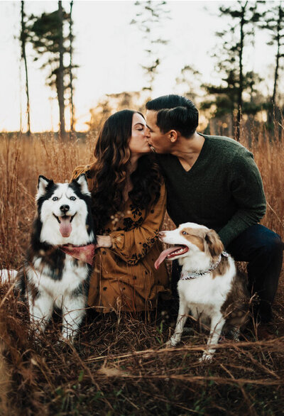 Couple kissing with happy pups in front of them