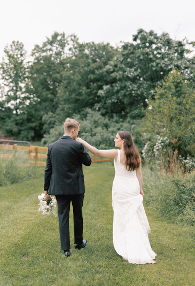 Bride and groom walk along a stone path with greenery around them. Bride is looking back at the groom .