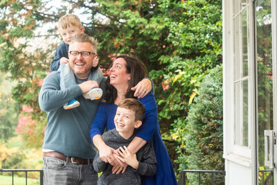 Parents smiling with one holding a small child on their shoulder and another child in front of them