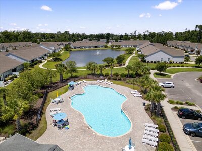 Aerial view of a community swimming pool surrounded by lounge chairs, and a pond with nearby homes
