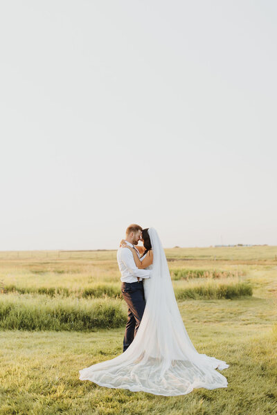 a bride and groom in a prairie field posing for their wedding photo