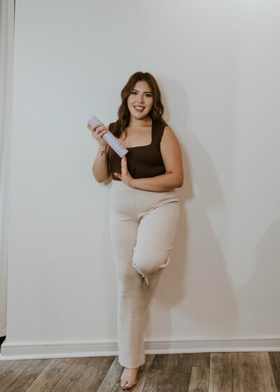 Graciella Mena, hairstylist at Heath Salon and Spa, smiling and holding a can of Pureology hairspray in her professional headshot, showcasing her product knowledge and fun personality.