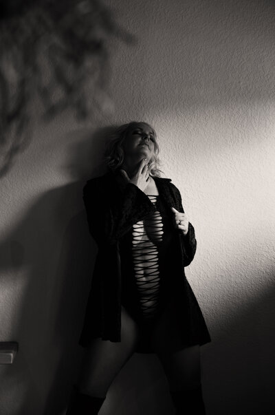 Woman standing confidently in black lingerie and robe, captured in dramatic lighting during a black and white boudoir session by Christie Newell.