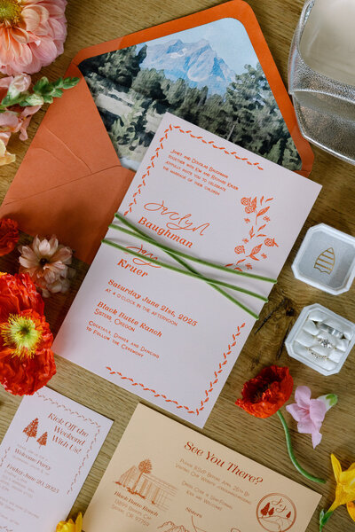 Pink and coral invitation flatlay featuring mountain details, envelope and florals representing full service design and calligraphy by Life in Letters.