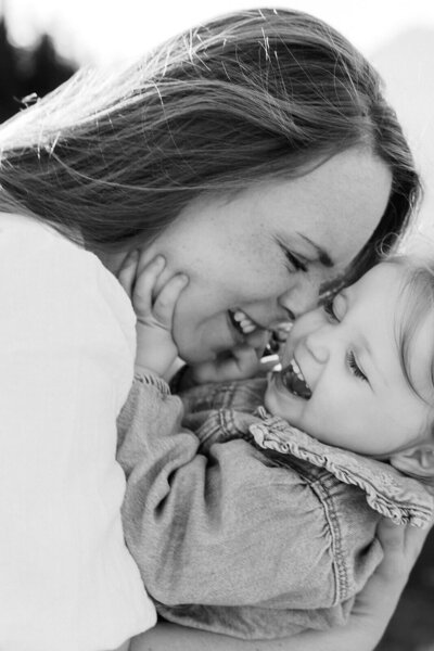 Schwarz-Weiß-Foto einer Mutter, die ihr lachendes Kleinkind liebevoll im Arm hält und an sich schmiegt.