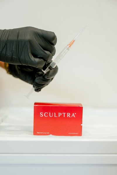 box of sculpra and needle getting tapped by nurse injector with black gloves 