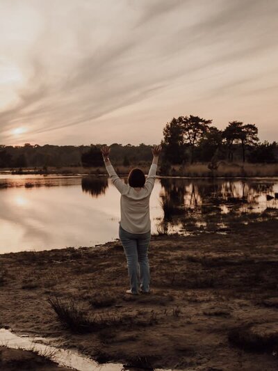 Enthousiaste fotograaf met armen omhoog aan het water bij zonsondergang