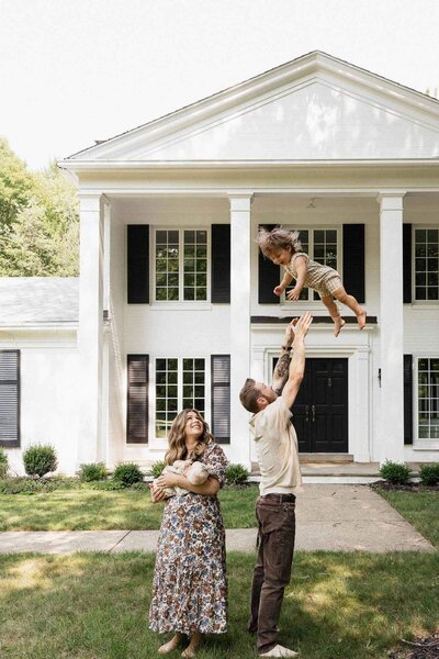 A playful outdoor moment from a Cleveland lifestyle newborn photography session, featuring a family enjoying time together on their front lawn.