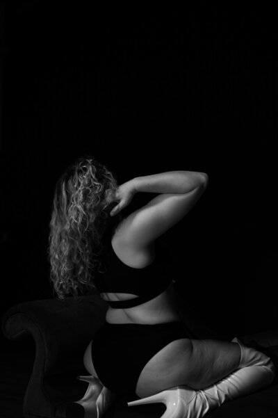 Black & White Boudoir photograph of Couch Boudoir pose  with one arm brushing hair off her shoulder.