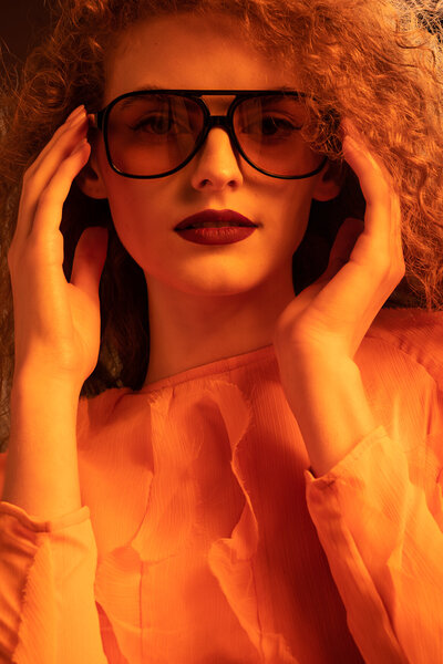 A woman wearing sunglasses looking straight to the camera wearing a orange dress