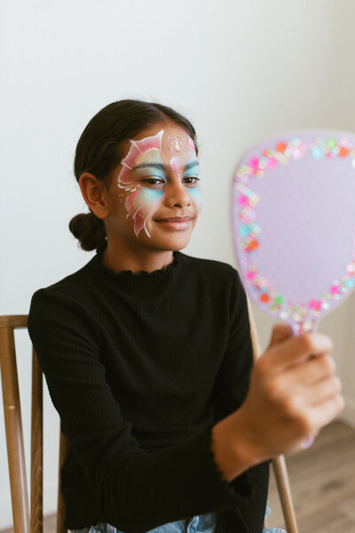 Girl with butterfly face paint looking in mirror