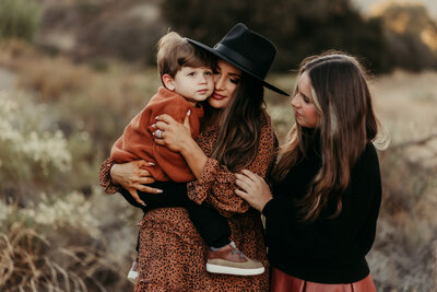 Mother holding her two young children during a cozy family photography session in Riverside County, California, dressed in warm earthy tones

