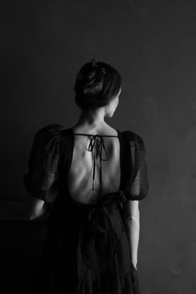 Black and white photo of the back of a woman in a black dress with her hair pinned up