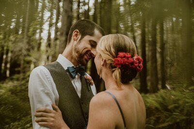 Bride and groom embracing with their faces close together under the canopy of a redwood forest grove in Northern California