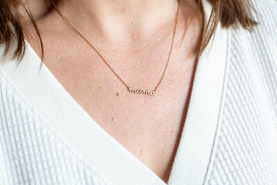 Close up of a woman wearing a mama gold script necklace