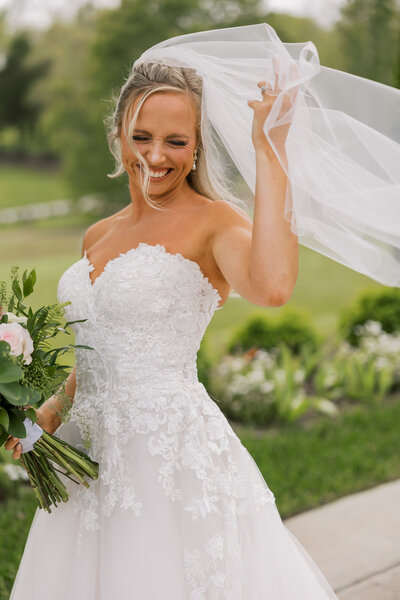 Bride in a candid moment as her long veil blows in the wind and she tries to catch it.