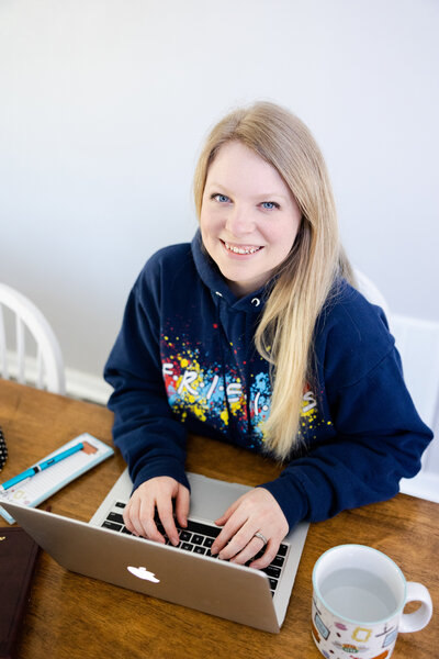 Photographer working on her computer at the kitchen table at home in Beavercreek, Ohio while taking notes and wearing a Friends sweatshirt.