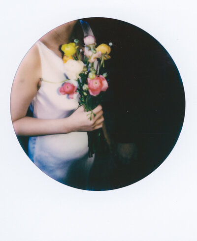 Polaroid photo of a bride holding a colorful spring bouquet, framed in close with soft film tones — a quiet wedding detail captured by a film wedding photographer.