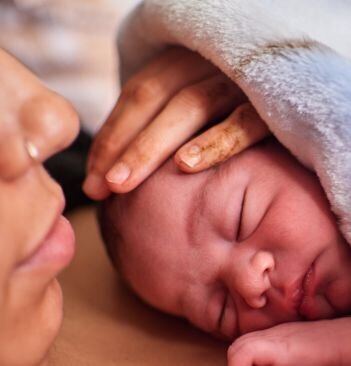 Baby doing skin to skin with their mother. The mother's hand is resting on the baby's head.