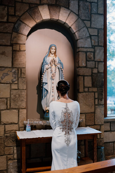 Catholic bride prays in front of statue of Mary before her wedding Mass.