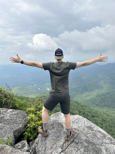 Person stands at the edge of a cliff with their hands raised