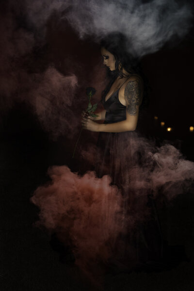 Woman wearing black dress outside at night with red smoke