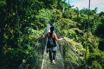 Traveler crossing hanging bridge in Costa Rican rainforest — luxury adventure travel for milestone celebrations.