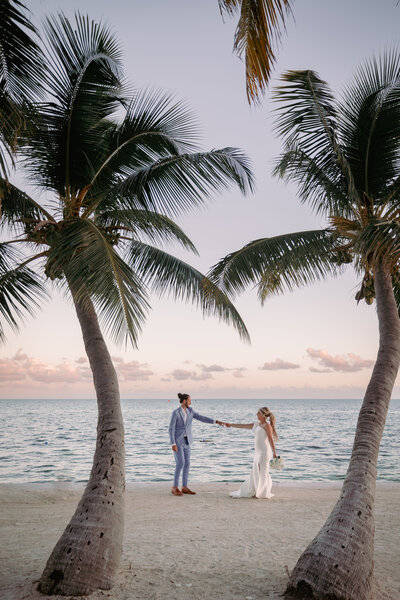 bride and groom holding hands while standing on the beach