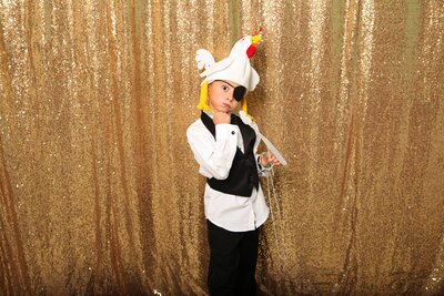Little kid in photobooth making a funny face and wearing a chicken hat