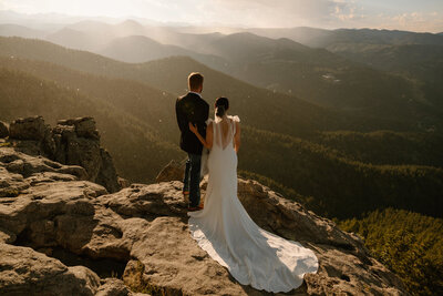 photo of bride and groom standing on a rock cliff overlooking the Colorado mountains taken by Colorado elopement photographer