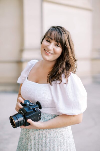 Woman with brown hair and bangs smiling while standing in front of a white building a portrait of Danielle Defayette