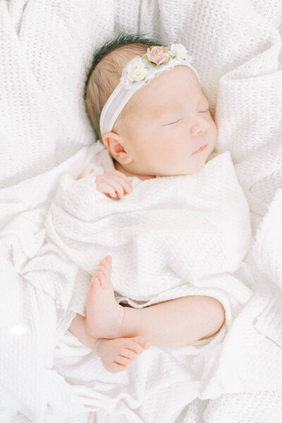 newborn baby girl with white bow wrapped in a white blanket with feet showing