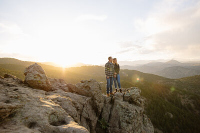 Boulder engagement session — a couple enjoying a quiet moment on big rocks, cracking open their favorite beers, with majestic mountain peaks and a golden sunset framing their love. Captured in an editorial, true-to-color style that showcases emotion and creative storytelling