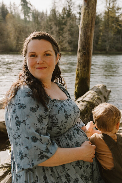 portland lifestyle photographer smiling at the camera at a river with a toddler