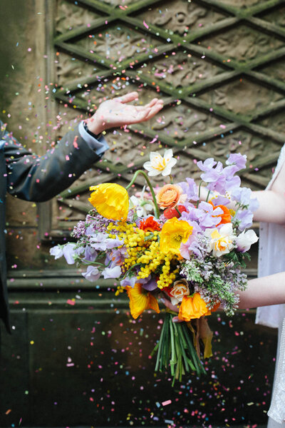 NYC Central Park elopement couple wearing Happy Isles vintage dress and colorful bouquet throwing confetti at Bethesda Terrace